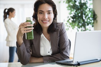 Hispanic businesswoman drinking green juice at desk in office