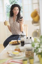 Mixed race woman using cell phone in kitchen