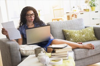 Mixed race woman paying bills on laptop on sofa