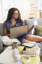 Mixed race woman paying bills on laptop on sofa