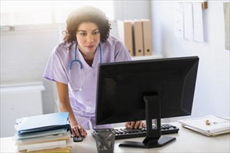 Mixed race nurse using computer in office