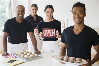 Caterers smiling together with food and open sign in event space