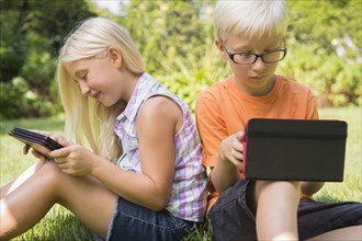 Caucasian children using digital tablets in backyard