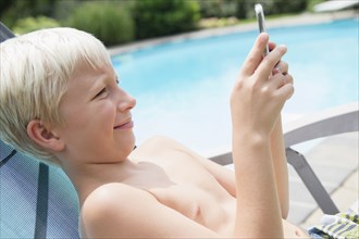Caucasian boy using cell phone near swimming pool