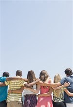 Rear view of teenagers hugging under blue sky