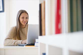 Caucasian teenage girl using laptop at desk