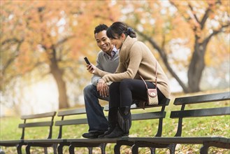 Couple using cell phone on park bench