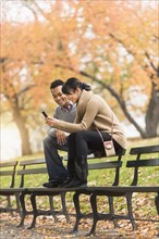 Couple using cell phone on park bench