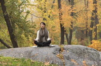 Asian woman meditating on rock in park