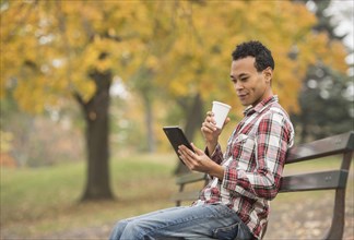 Mixed race man using digital tablet on park bench