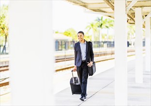 Black businessman rolling luggage on train platform