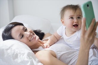 Mixed race mother playing with baby and cell phone on bed
