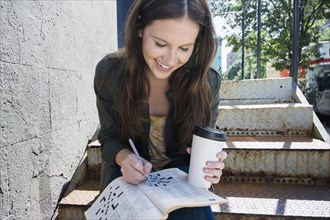 Caucasian woman doing crossword and drinking coffee on front steps