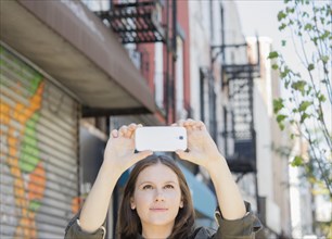 Caucasian woman taking cell phone photograph on urban sidewalk