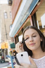 Caucasian woman applying makeup in cell phone camera