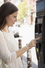 Caucasian woman using parking meter on urban sidewalk
