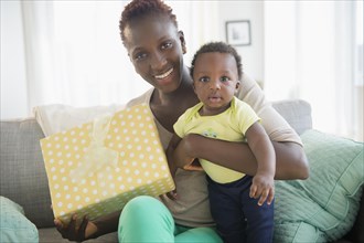 Black mother and son holding gift on sofa