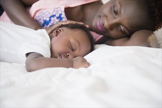 Black mother admiring sleeping son on bed