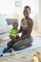 Black mother holding baby boy on exercise mat in living room