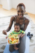 Black mother holding baby boy and eating salad