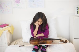 Pouting Vietnamese girl holding violin in bedroom