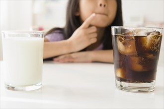 Vietnamese girl choosing between glass of soda and milk