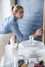 Caucasian barista writing menu on cafe chalkboard