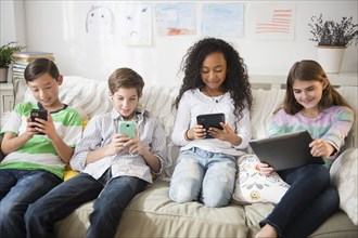 Children using cell phones and digital tablets on sofa