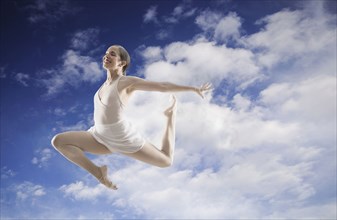 Hispanic dancer leaping in cloudy blue sky