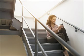 Low angle view of mixed race businesswoman using cell phone on staircase