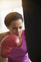 Mixed race woman hitting punching bag in gym