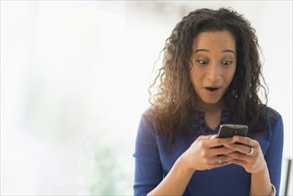 Close up of mixed race woman gasping at cell phone