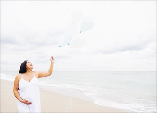 Pregnant mixed race woman holding balloons on beach