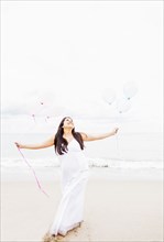 Pregnant mixed race woman holding balloons on beach