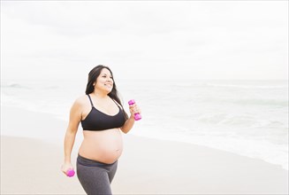 Pregnant mixed race woman exercising on beach