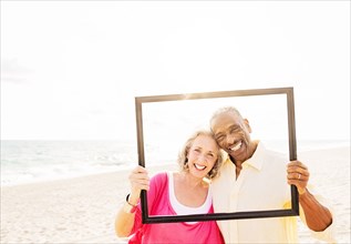 Older couple posing in picture frame on beach