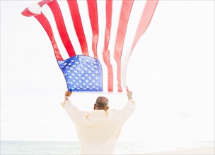 Older mixed race man holding American flag on beach
