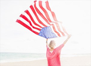 Older Caucasian woman holding American flag on beach
