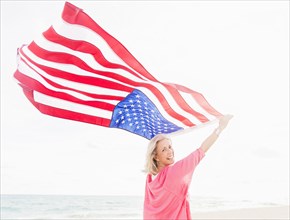 Older Caucasian woman holding American flag on beach