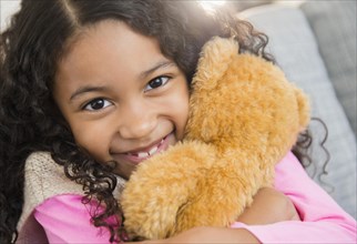 Mixed race girl hugging teddy bear on sofa