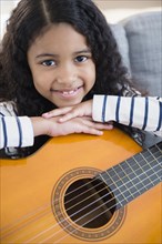 Mixed race girl holding guitar on sofa