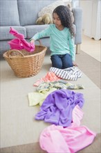 Mixed race girl sorting laundry on living room floor