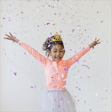 Mixed race girl wearing tiara throwing confetti