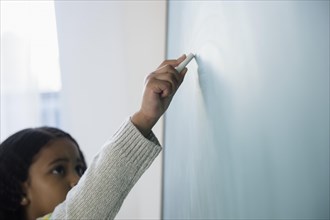 Mixed race student writing on chalkboard in classroom