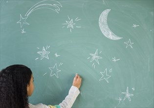 Mixed race student drawing stars on chalkboard in classroom