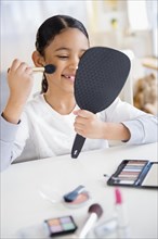 Mixed race girl applying makeup with brush