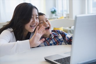 Brother and sister waving at video chat on computer