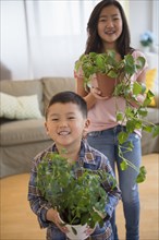Asian brother and sister holding potted plants in living room