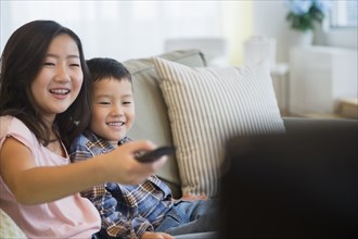 Asian brother and sister watching television on sofa