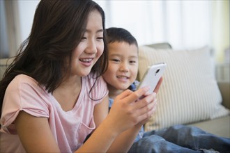 Asian brother and sister using cell phone on sofa